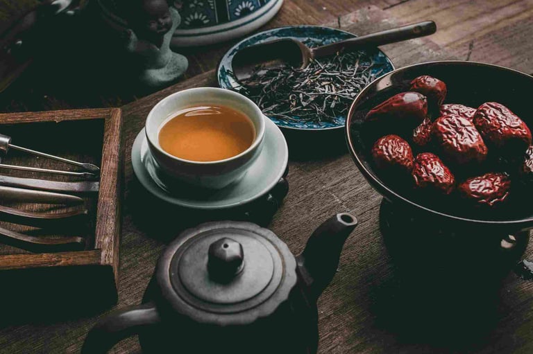 Rustic tea scene with teacup, black teapot, dried dates and loose leaves