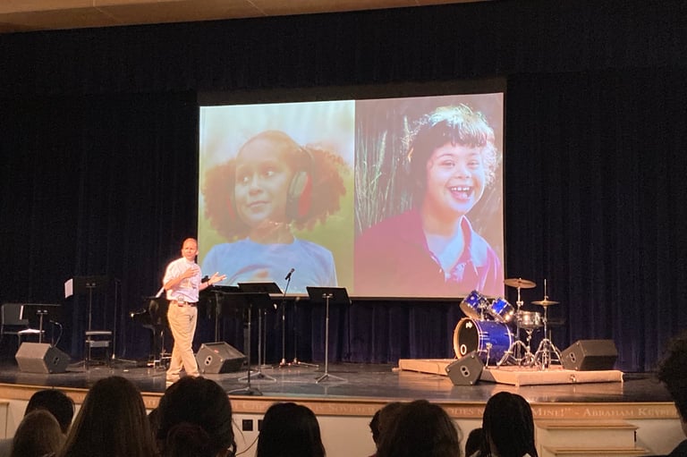 a man standing on a stage with a video screen showing a video of a woman