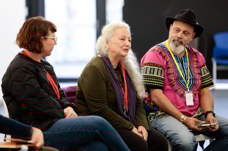 Three people seated on chairs. The person in the middle is speaking and the other two listen closely