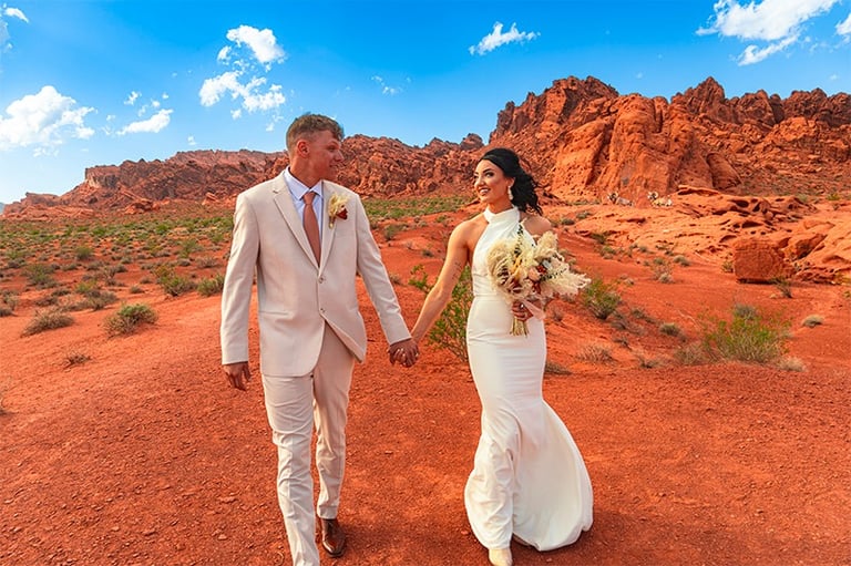 a bride and groom walking down a dirt road