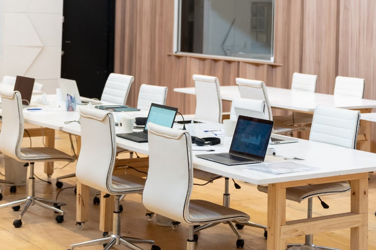 Modern shared office space with white ergonomic chairs, wooden desks, and laptops for co-working.