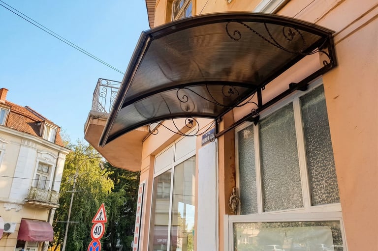 Curved bronze polycarbonate door awning with decorative wrought iron brackets on a city building.