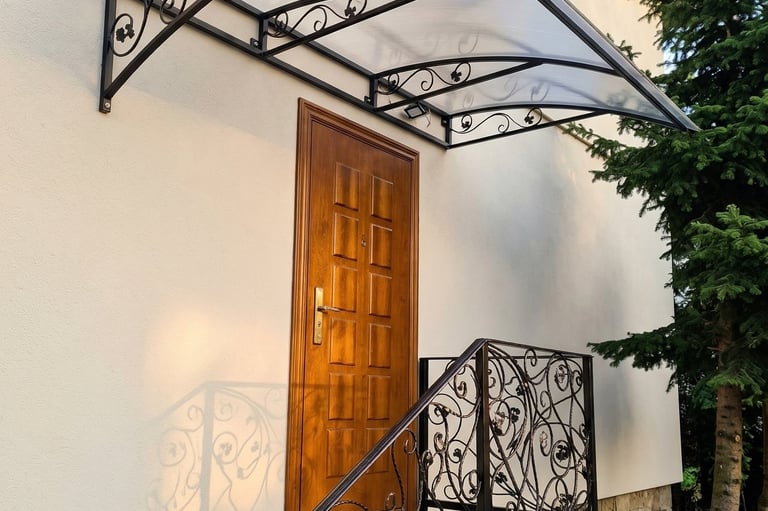 Elegant wrought iron door canopy with polycarbonate roof over a wooden entrance door and matching railing.