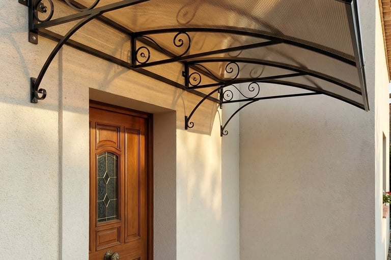 Modern door canopy with wrought iron scroll brackets and bronze polycarbonate roof over a wooden front door.