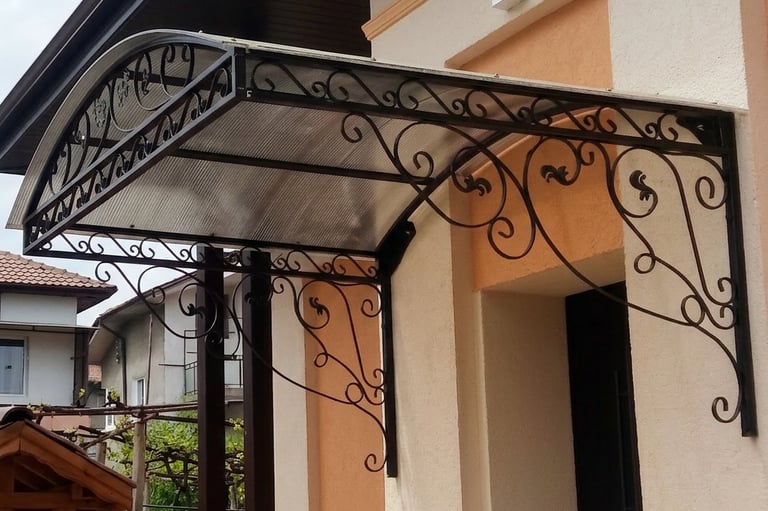 Ornate black wrought iron door awning with polycarbonate roof installed over a home entrance.