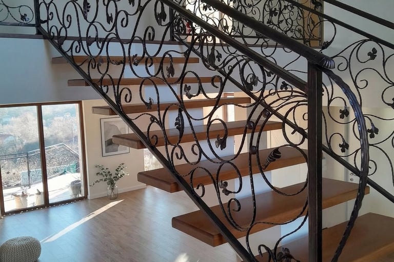 Modern floating wooden staircase featuring ornate wrought iron scrollwork railings in a bright, sunlit home.