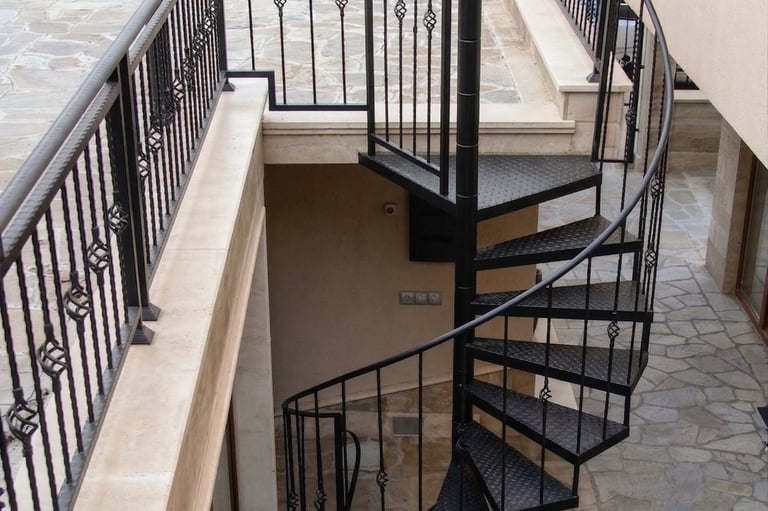 Black outdoor metal spiral staircase with decorative wrought iron railings leading to a stone patio.