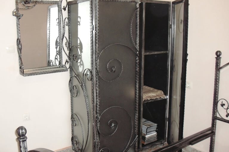 Custom wrought iron wardrobe with ornate scrollwork, matching wall mirror, and gothic metal bed frame.