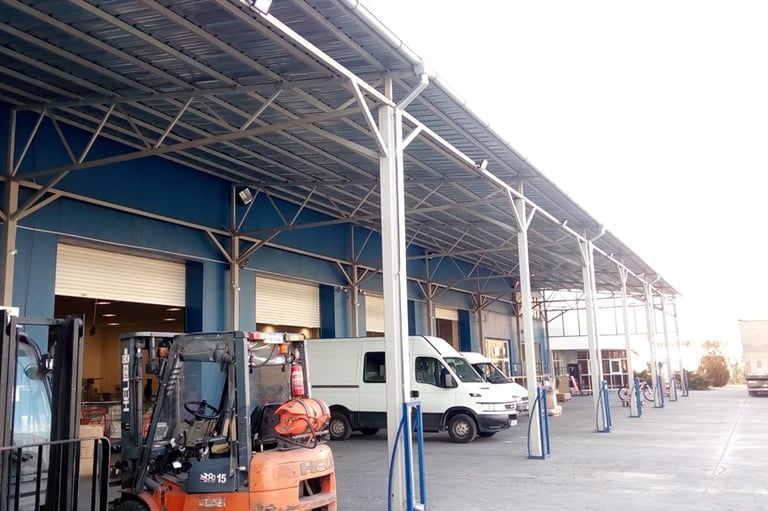 Logistics warehouse loading dock with parked forklifts, delivery vans, and a metal canopy.