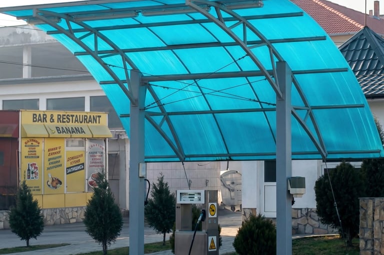 A single gas pump station under a curved blue polycarbonate canopy near a restaurant.