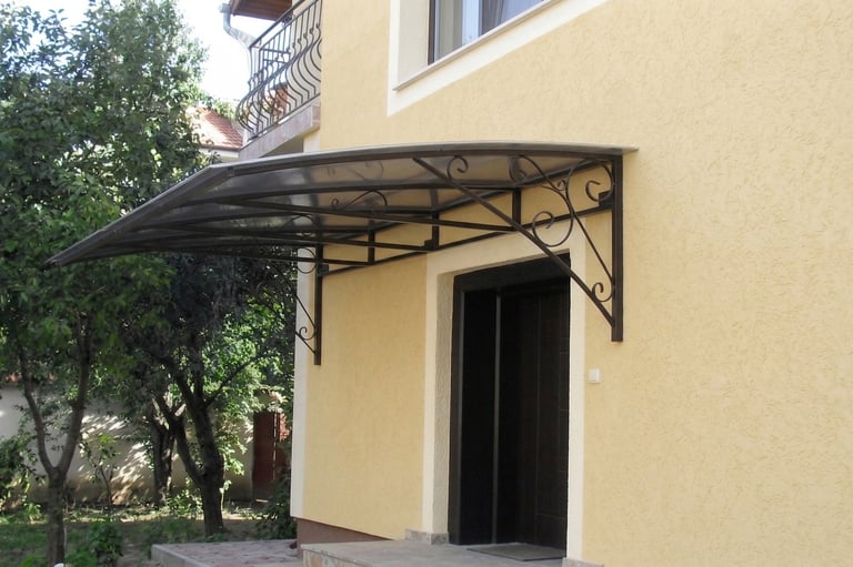 A curved wrought iron door canopy with a clear polycarbonate roof installed over a house entrance.