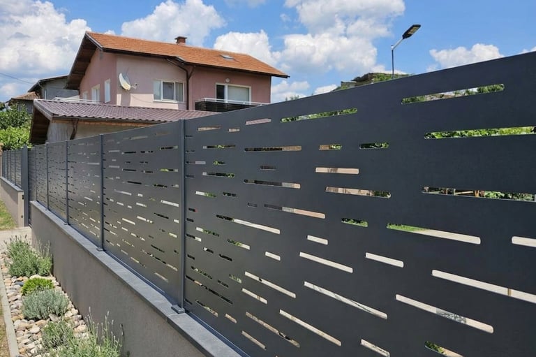 Modern anthracite laser-cut metal privacy fence installed on a concrete wall in a residential garden.