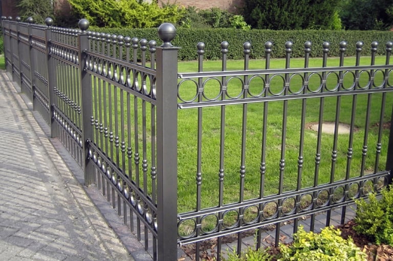 Black ornamental wrought iron fence with decorative circles and finials surrounding a green garden lawn.