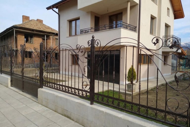 Custom decorative wrought iron fence and gate surrounding a modern two-story residential house.