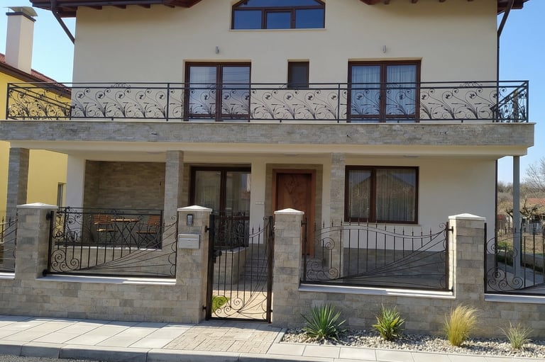 Modern two-story house with elegant wrought iron balcony railings and a matching stone garden fence.