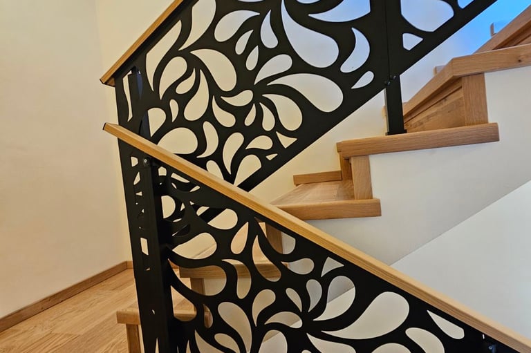 Modern wooden staircase featuring decorative black laser-cut metal railings with a floral swirl pattern.