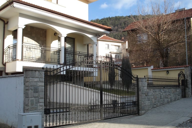 Modern white house with a decorative wrought iron gate and stone pillar fencing.