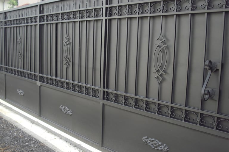 Elegant black ornamental wrought iron driveway gate with decorative scrollwork and a solid privacy base.