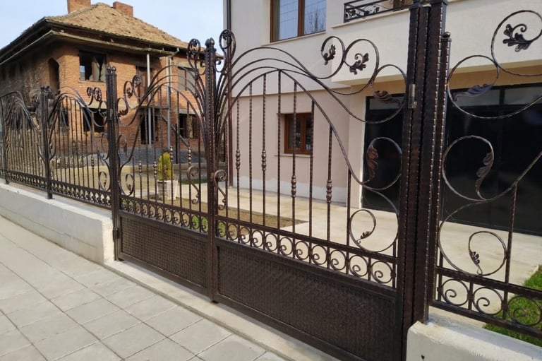 Elegant dark brown wrought iron driveway gate and matching fence with ornate scrollwork details.