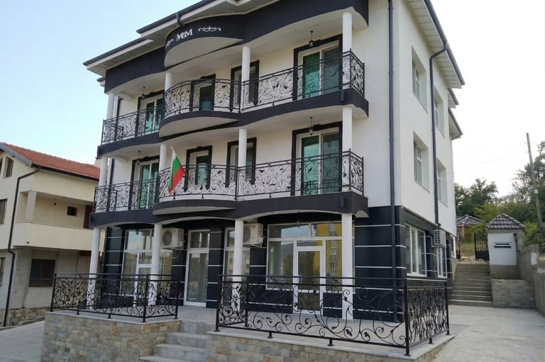 Modern white and black three-story apartment building with ornate wrought iron balconies and a Bulgarian flag.