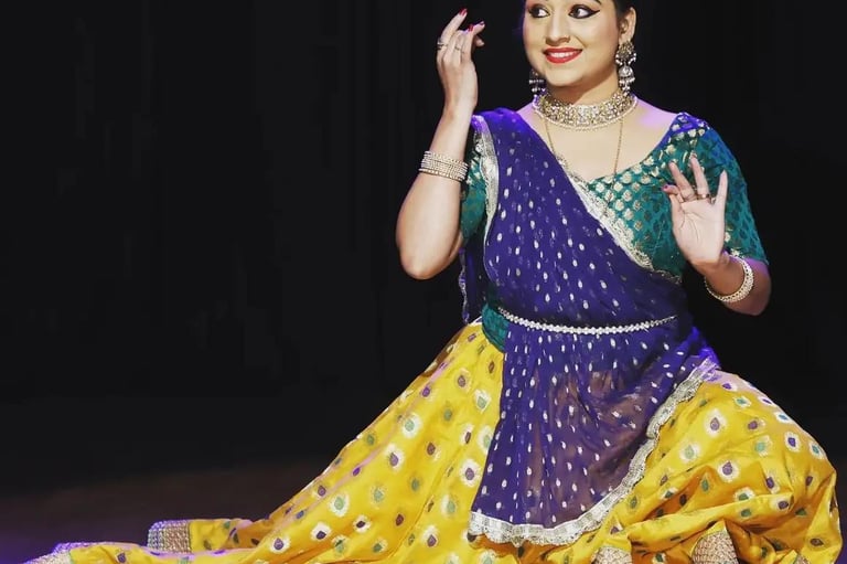 A Kathak dancer performing in traditional yellow and blue attire with ornate Indian jewellery.