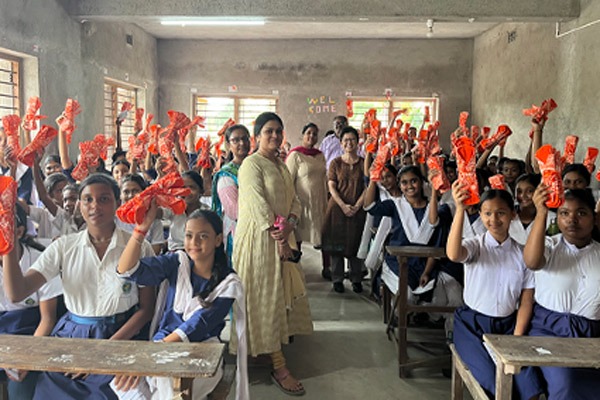 Large classroom of girls holding up napkin packs. with teachers