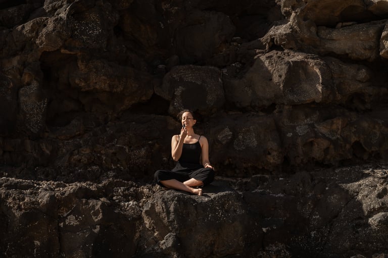 Yogalehrerin Martina Riedl in schwarzen Felsen sitzend und an ätherischem Öl riechend.
