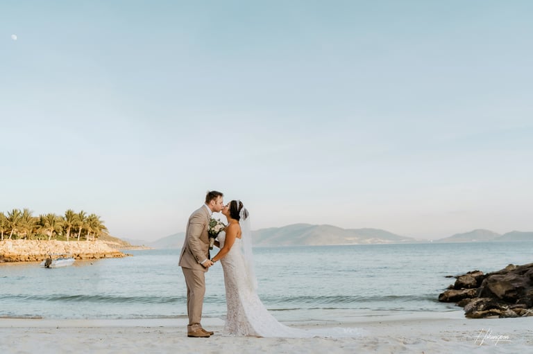 a bride and groom kissing on the beach