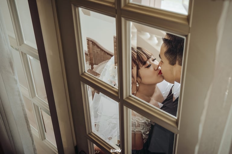 a bride and groom kissing in front of a window