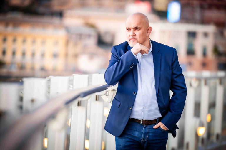 Henrick Photo in a navy blue blazer and jeans standing on the deck of a cruise ship at sunset