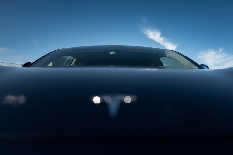 Low‑angle front view of an electric car’s hood TESLA and windshield under a blue sky, By ACAT Photos