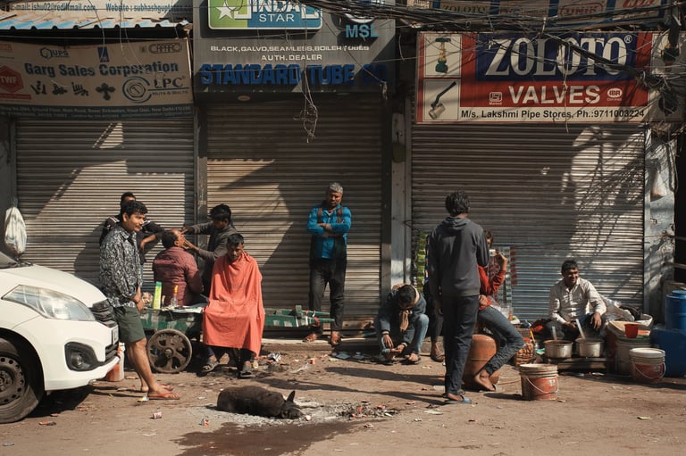 Street barber and locals gathered outside shuttered shops in Old Delhi