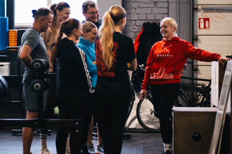 A diverse group of athletes talking to a female coach in a CrossFit gym during a fitness workout.