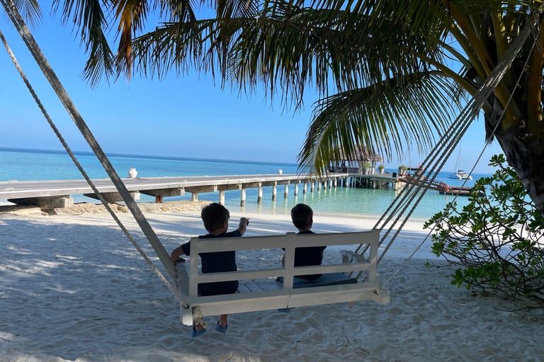 two people sitting on a swing chair in the sand