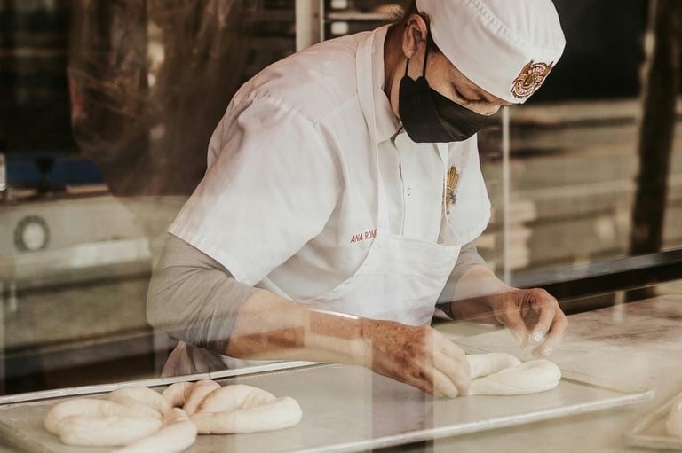 Panadero profesional con uniforme blanco y cubrebocas dando forma a masa fresca sobre una bandeja pa