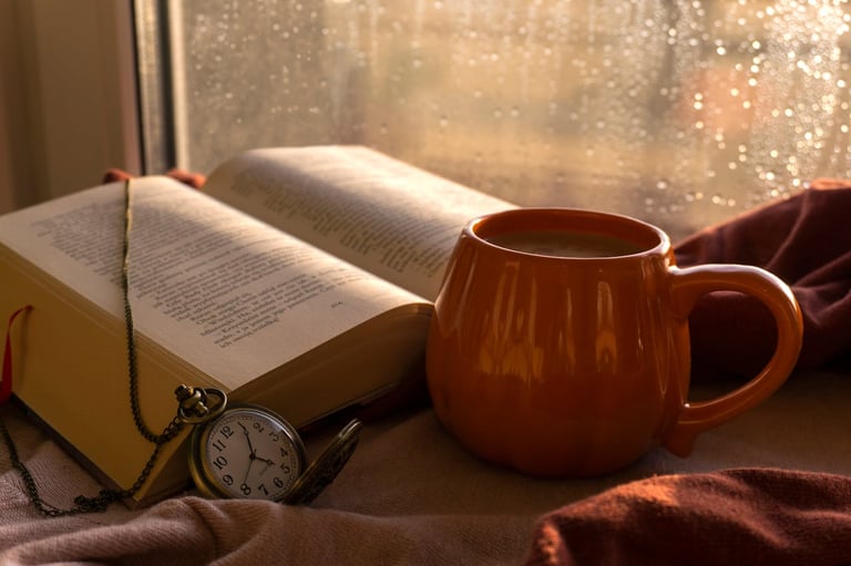 Open book and a warm drink by a rainy window creating a calm rainy mood.