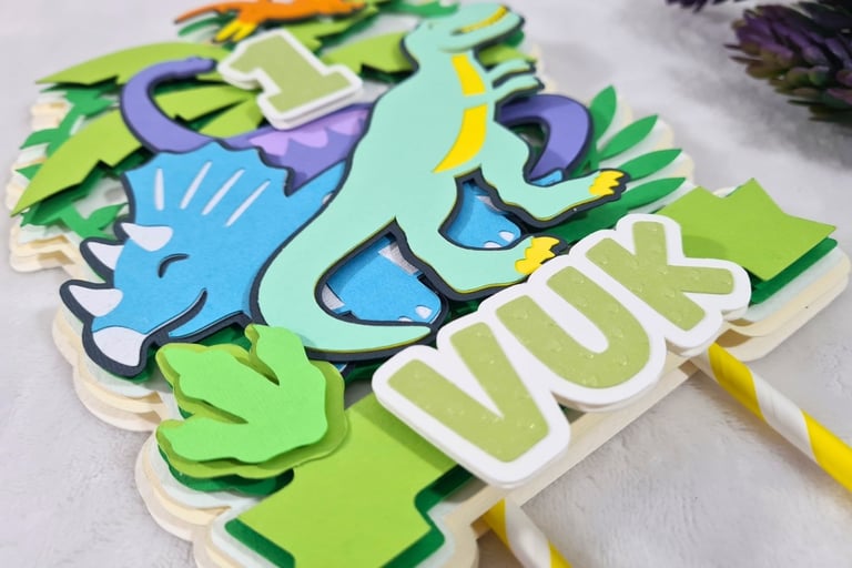Colorful paper cake topper featuring a cartoon dinosaurs theme with the number "1" at the center. Th