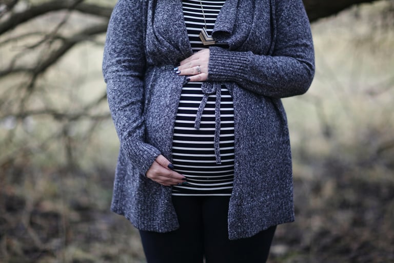 a pregnant woman wearing a striped shirt and a blue cardigan holding her belly