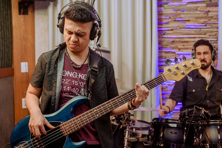 Bassist Ian Yoshio wearing a dark denim shirt and headphones, playing a navy blue Sterling bass guitar with drummer Lucas Dia
