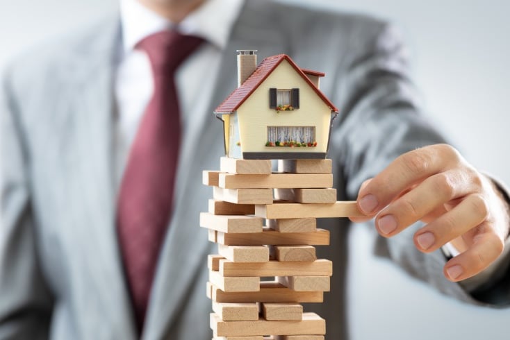 Stack of wooden blocks with a small house on top and a person's hand, symbolizing real estate invest