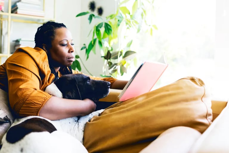 Una mujer afro sentada en un sofá con un perro y leyendo
