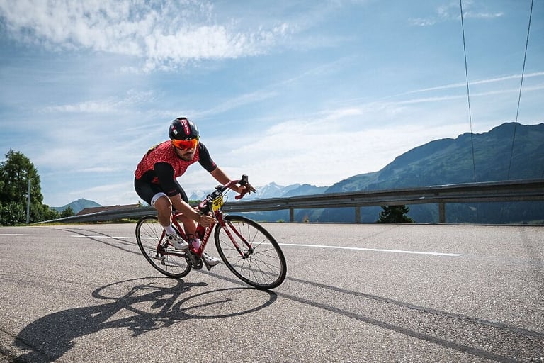 Un cycliste rouge se penche dans un virage dans un col des Alpes