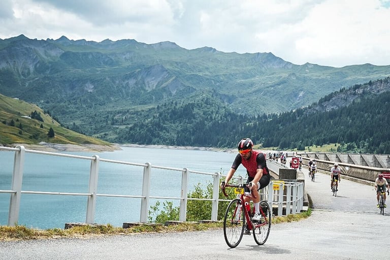 Un cycliste habillé en rouge trverse un barrage dans les Alpes, entouré de montagne