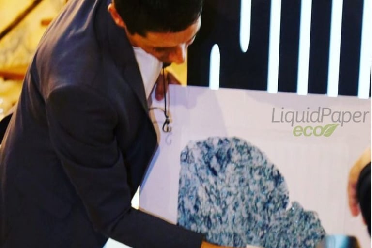 HOMEM DE TERNO ESCURO APLICANDO O PAPEL DE PAREDE LIQUIDO COM A BASE DE PVC BRANCO COM A LOGO
