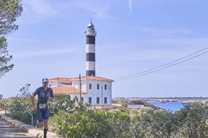 a man running on a path with a lighthouse in portocolom