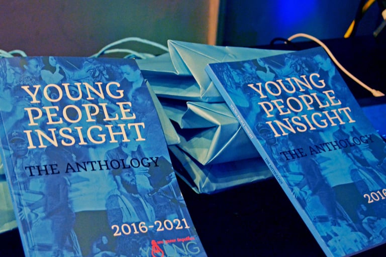 two books with blue covers, and white and black text people, balanced on blue bags on a table