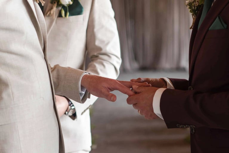 man slides ring onto his husbands hand on their wedding day