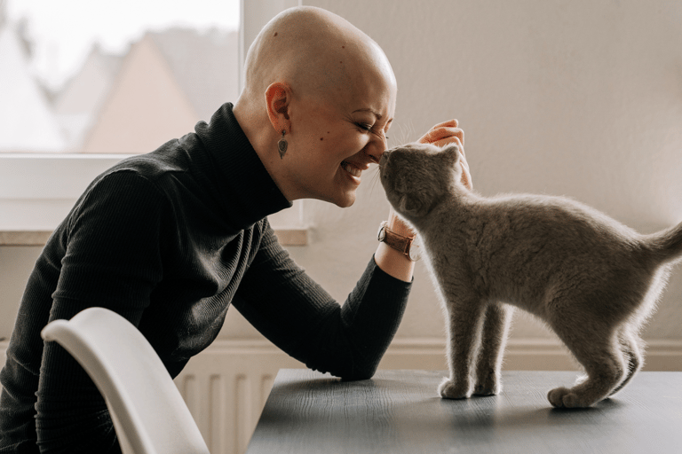 Bald woman in a turtle neck is petting her grey cat and getting acupuncture for cancer side effects