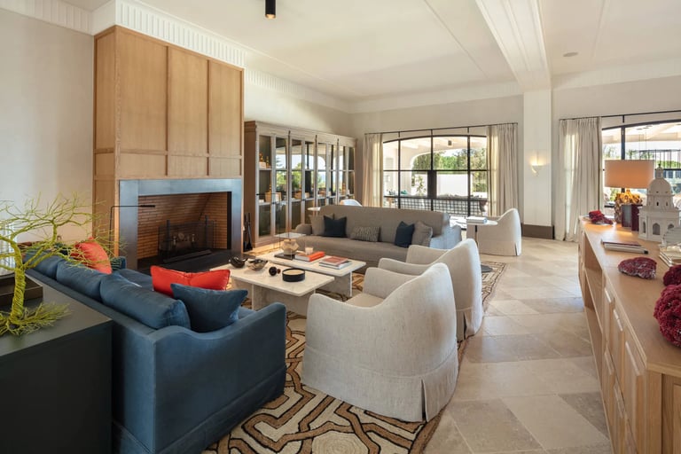Seating area at Villa La Gratitud with designer sofas, fireplace, and garden views through windows. 