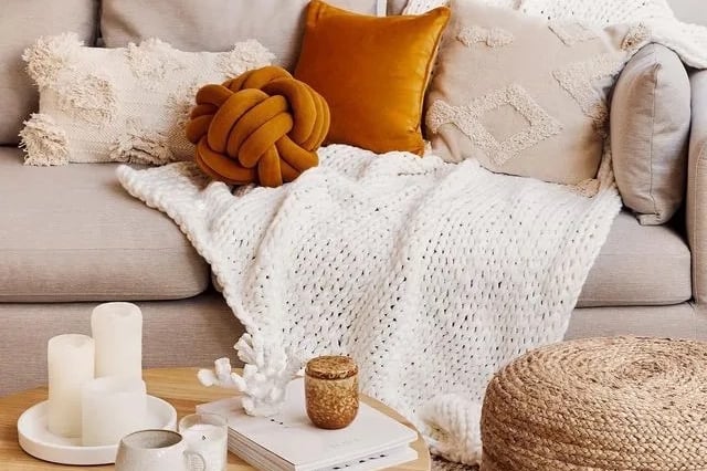 Couverture et coussins dans les tons beige et orange posés sur un canapé